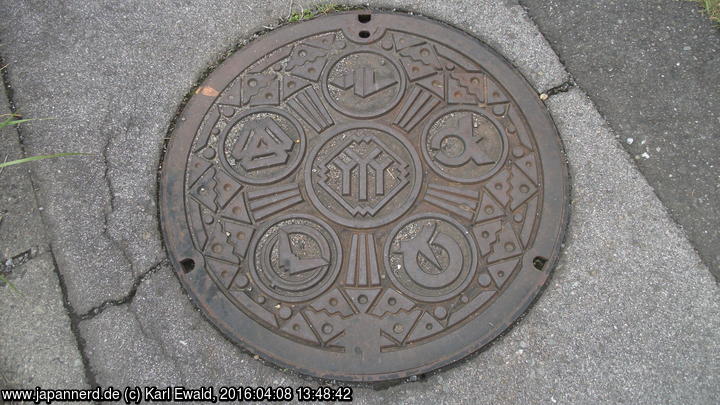 Klick für Großformat Kanaldeckel mit mehreren Logos, rechts das von Ôtsuki City.