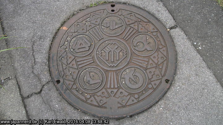 Kanaldeckel mit mehreren Logos, rechts das von Ôtsuki City.
